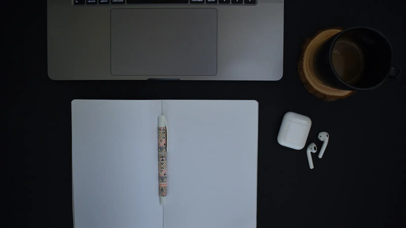 A tidy desk with a laptop, notebook and coffee