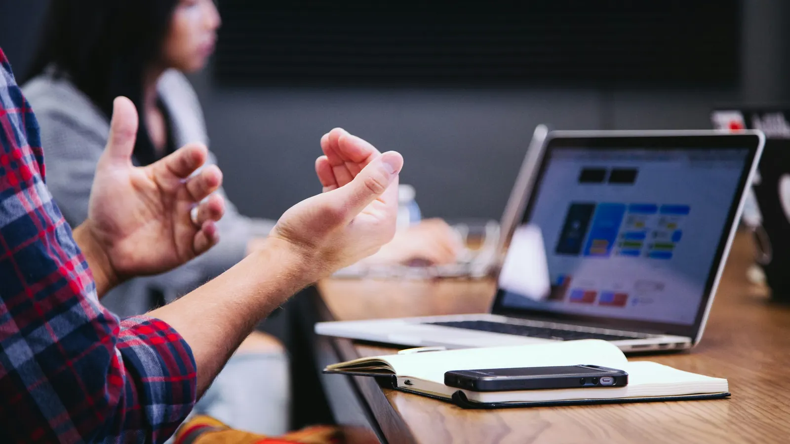 A person gesturing in a meeting beside an open laptop